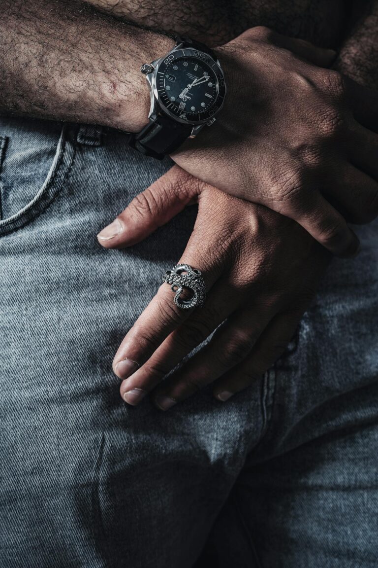 Close-up of a man's hands wearing a wristwatch and unique ring, emphasizing style and fashion.