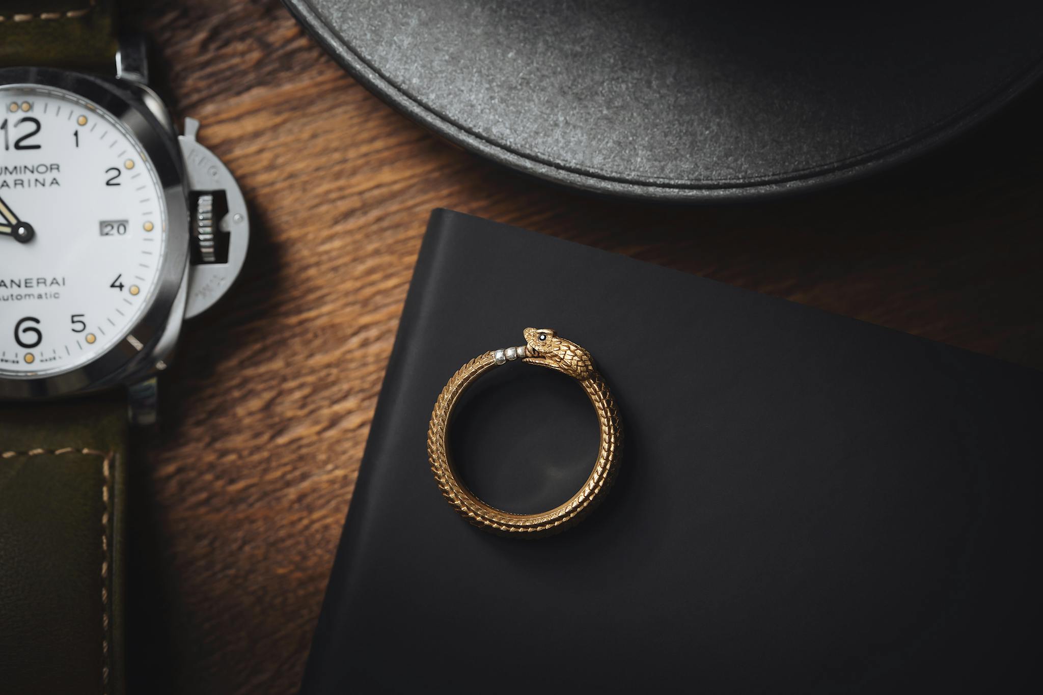Close-up of a stylish snake ring and luxury wristwatch on a dark wooden surface.
