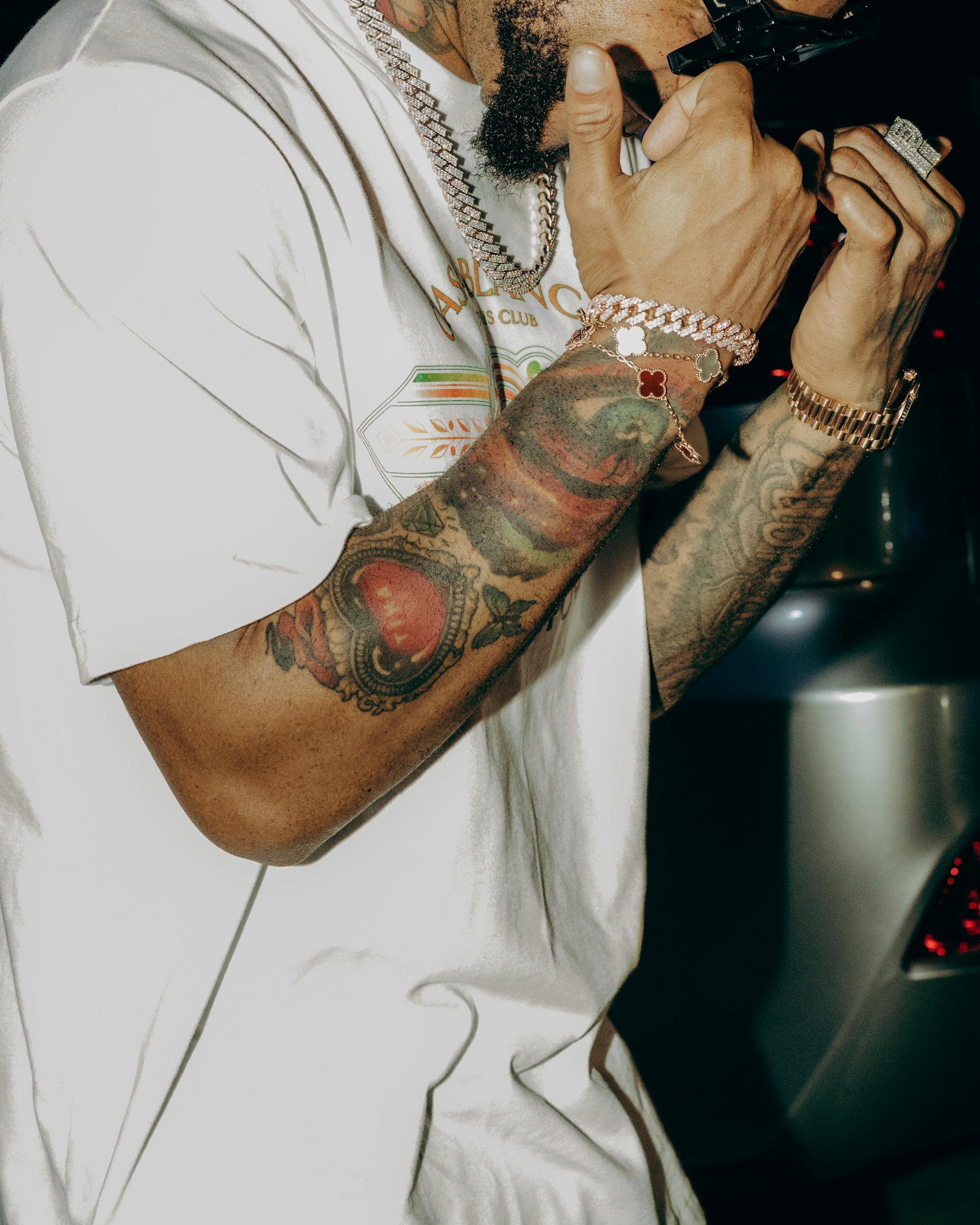Close-up of a stylish tattooed man holding sunglasses at night.